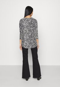 Svart och vit djurmönstrad topp med trekvartsärmar, avslappnad passform och rundad nederkant, tillsammans med utsvängda svarta byxor och klackstövlar.