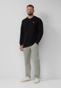 Black long-sleeve sweatshirt with a crew neck and a small logo on the chest, paired with light green pants and white sneakers.
