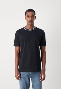 Juodas medvilninis marškinėlis su apvalia iškirpte, turintis baltą juostelę ir "BOSS" logotipą. Trumpomis rankovėmis ir reguliaraus kirpimo, derinamas su mėlynomis džinsinėmis kelnėmis.