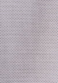 Gros plan sur un tissu texturé avec des petits points circulaires marron uniformément espacés sur un fond beige clair.