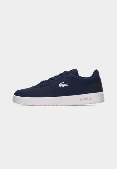 Тъмносиня спортна обувка на Lacoste с бяла гумена подметка и бял крокодилски лого отстрани, показана в профил на светъл фон.