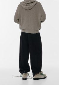 Hoodie gris clair côtelé avec capuche, associé à un pantalon noir ample et des chaussures beiges texturées avec des lacets verts, vu de dos.