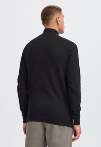 Pulover negru cu guler înalt, confecționat dintr-un material tricotat moale, având mâneci lungi, un tiv elastic și o croială lejeră.