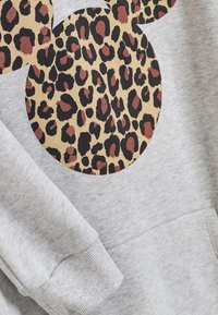 Šedá mikina s velkým designem kruhu s leopardím potiskem v béžové, černé a burgundské barvě. Obsahuje přední kapsu a žebrované manžety.