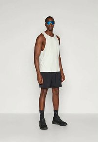 Hellgraues ärmelloses Tanktop mit strukturiertem Muster, kombiniert mit schwarzen Shorts. Die Accessoires umfassen blaue Sonnenbrillen und schwarze Sportschuhe.