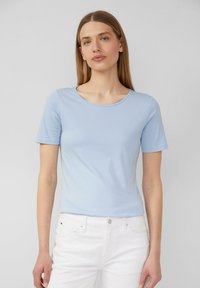 T-shirt en coton bleu clair à manches courtes et col rond, associé à un jean blanc, avec une texture lisse et une coupe décontractée.