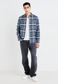Camisa a cuadros azul con líneas blancas y marinas, sobre una camiseta blanca, combinada con jeans grises y zapatillas blancas.