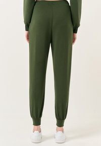 Groene joggingsbroek van zacht materiaal, met elastische boorden en een tailleband. Gecombineerd met witte sneakers voor een casual uitstraling.