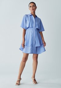 Blau-weiß gestreiftes Hemdkleid mit einem geknöpften Kragen, kurzen Ärmeln, tailliertem Schnitt und asymmetrischem Saum. Glatte Stofftextur.