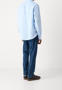Camicia a maniche lunghe di colore azzurro chiaro, realizzata in tessuto morbido, abbinata a jeans in denim blu scuro. L'outfit è completato da sneakers nere casual.