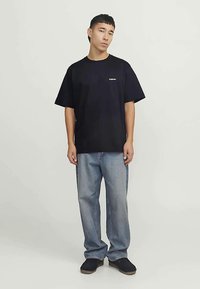 Mustast puuvillast lühikeste varrukatega T-särk ümmarguse kaelusega, millel on rinnal väike valge logo, kombineeritud helesiniste teksapükstega.