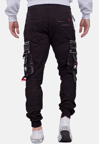 Schwarze Cargo-Hose mit mehreren Taschen, verstellbaren Bündchen und Kontrastnähten. Verfügt über Hardware-Details und ein strukturiertes Material.