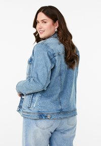 Šviesiai mėlynas džinsinis švarkas su dviem priekinėmis kišenėmis, mygtukų uždarymu ir nusidėvėjimo akcentais. Turi standartinį apykaklę ir laisvą iškirpimą.