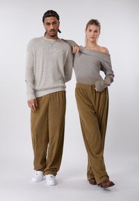 Δύο μοντέλα φορούν casual ρούχα: το ένα με ανοιχτό γκρι πουλόβερ με κέντημα και φαρδιά καφέ παντελόνια από κοτλέ· το άλλο με τοπ ριμπ σε τόνο ταουπ που αφήνει τους ώμους ακάλυπτους.