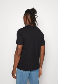 Černé bavlněné tričko s krátkými rukávy, kulatým výstřihem a jednoduchým designem, nošené s světle modrými džínami. Žádné viditelné vzory nebo akcenty.