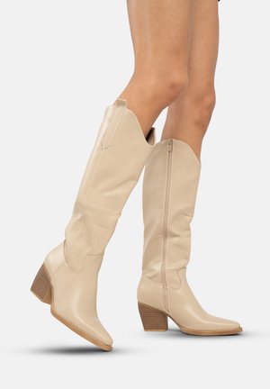 Beige leren laarzen tot de knie met een puntige neus en een gestructureerde blokhak. Voorzien van een zijrits en een gebogen bovenzijde.