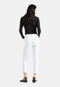 Un haut noir à manches longues, un jean blanc taille courte, et des chaussures plates noires. Les jeans comportent des poches arrière et un design ajusté.