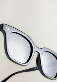 Lunettes de soleil noires et argentées avec une finition brillante, présentant une forme géométrique et des verres miroités. Design minimaliste avec des accents matériels subtils.