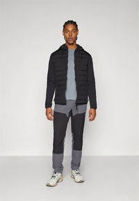 Melna pūkaina jaka ar kapuci, pelēks garroku krekls un pelēkas-melnas bikses. Pastiprinātas ceļgalu detaļas un gaišas sporta kurpes.