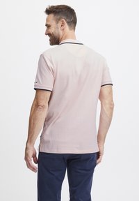 Rövid ujjú, világos rózsaszín pamut poloing, tengerészkék gallérral és ujjak szegésével. Oldalsó hasítékokkal és márkás díszítésekkel a szegés közelében.