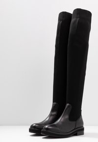 Botas negras hasta la rodilla con una punta de cuero y un tubo elástico de punto texturizado. Suela de goma con un ligero tacón.