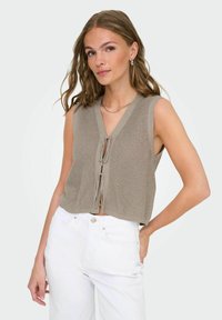 Khaki strikket crop-top med V-udskæring og frontbindinger. Har ærmeløs design og tekstureret stof. Sættes sammen med hvide jeans.