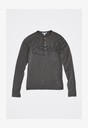 Donkergrijs henley-shirt met lange mouwen, vier knopen en grote cursieve tekst "Blessed" over de borst.