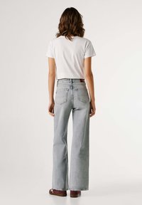 Jeans gris claro de talle alto con piernas anchas, combinados con una camisa blanca de manga corta. Los zapatos son de color burdeos con detalles blancos.