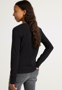 Langærmet sort T-shirt med rund hals. Blødt, strækbart stof. Sættes sammen med grå jeans, der viser en tætsiddende silhuet.
