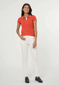 Rode polo met witte accents, drie-knopen sluiting, gecombineerd met witte slim-fit jeans en marineblauwe instappers. Eenvoudig en getailleerd ontwerp.