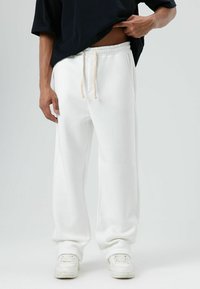 Witte joggingbroek met elastische tailleband en trekkoord, voorzien van zijzakken en een relaxte pasvorm. Gecombineerd met witte sneakers.