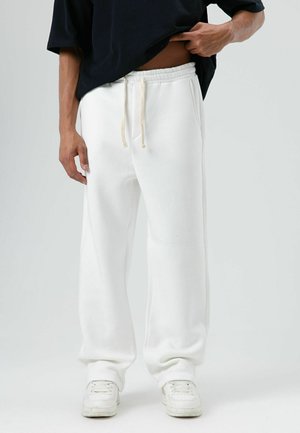 Witte joggingbroek met elastische tailleband en trekkoord, voorzien van zijzakken en een relaxte pasvorm. Gecombineerd met witte sneakers.