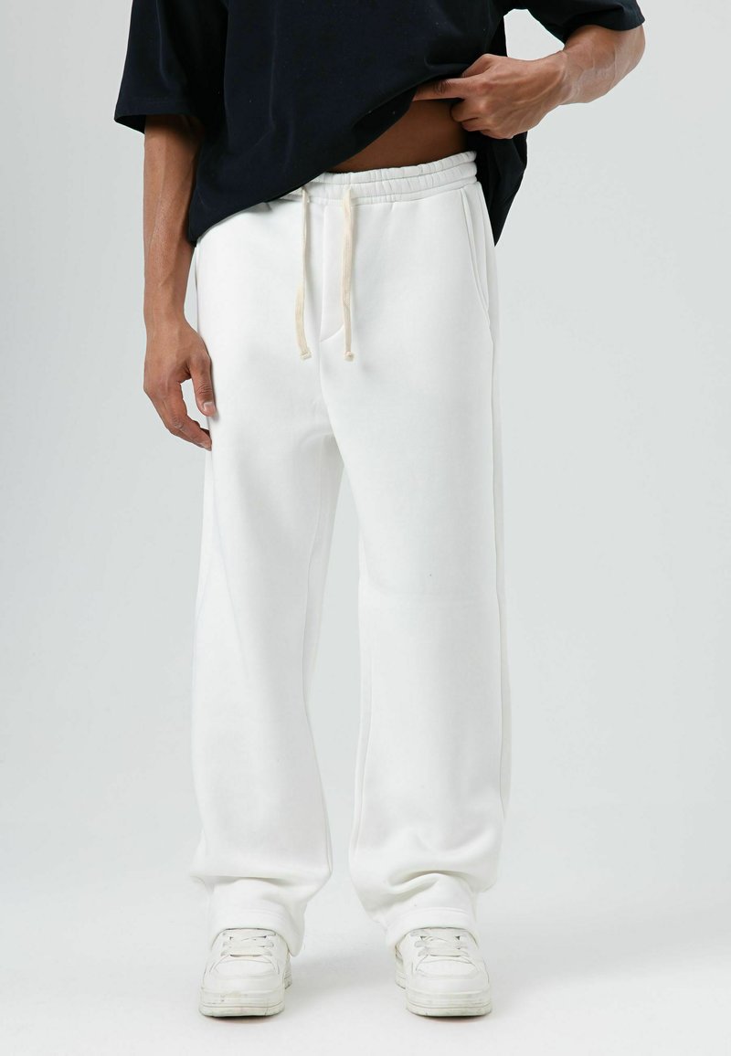 Witte joggingbroek met elastische tailleband en trekkoord, voorzien van zijzakken en een relaxte pasvorm. Gecombineerd met witte sneakers.