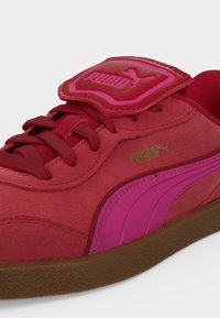 Κόκκινο και ροζ αθλητικό παπούτσι Puma με καφέ σόλα, με λεπτομέρειες το λογότυπο Puma στο πλευρό και στην γλώσσα, με κόκκινα κορδόνια και υφή σουέτ.
