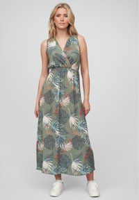 Green floral maxi dress with a v-neck and sleeveless design, featuring a tropical leaf print in blue, white, and rust colors, paired with white sneakers.