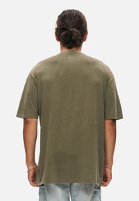 Olivi vihreä puuvillapaita lyhythihaisilla hihoilla, rento malli ja suora helma. Takana kaula-aukon kohdalla pieni printti.