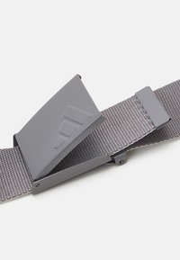 Grå stofrem med en mat grå metalspænde, der har et geometrisk design. Tekstureret overflade og solid konstruktion er synlige.