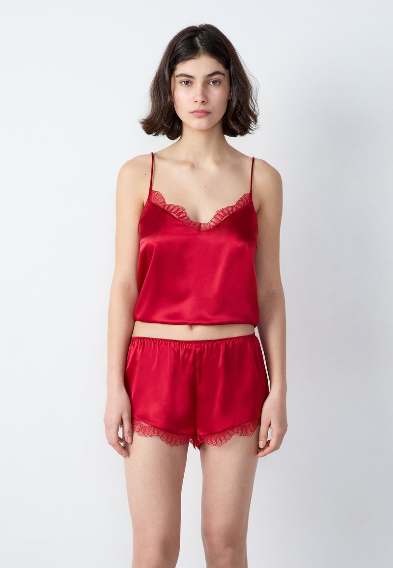 Rode satijnen pyjama set met een mouwloos topje met kanten afwerking en bijpassende shorts met golvende kanten accenten, zachte textuur.