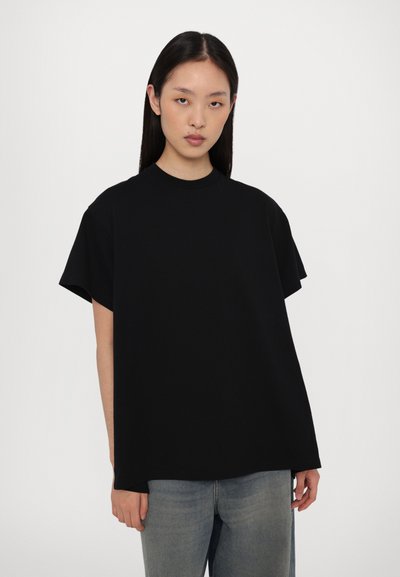 T-shirt nera oversize con collo a girocollo realizzata in misto cotone, con maniche corte e vestibilità rilassata, abbinata a jeans azzurri chiari.