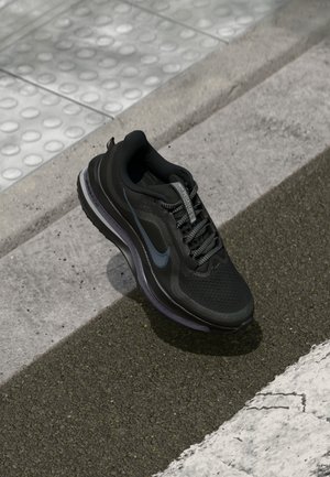 Schwarzer Sportschuh mit blauem Nike-Logo auf Asphalt nahe dem Bordstein und strukturiertem taktilem Belag.