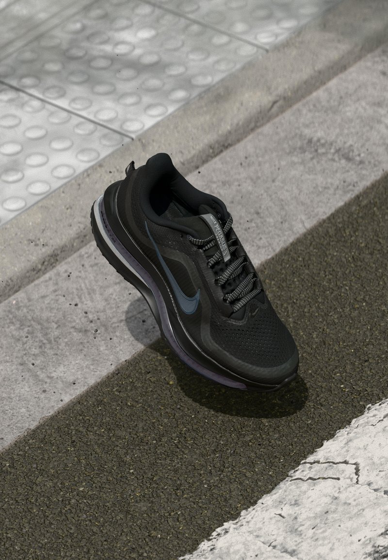 Baskets de sport noires avec logo Nike bleu sur asphalte près du trottoir et surface tactile texturée.
