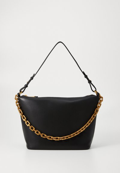 Bolso de mano de cuero negro con una forma estructurada, que presenta una asa de cadena dorada gruesa y una correa de hombro delgada desmontable. Cierre con cremallera.