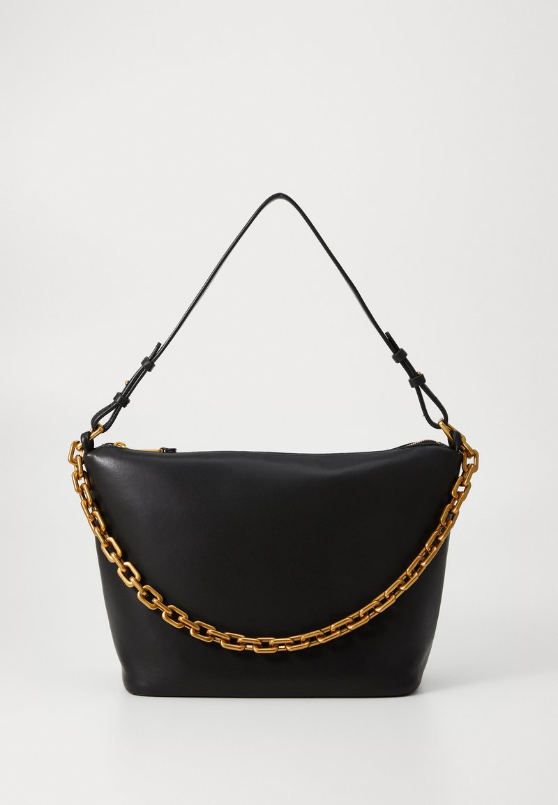 Bolsa de mão em pele negra com uma forma estruturada, apresentando uma alça em corrente grossa dourada e uma alça de ombro fina destacável. Fecho em zíper.