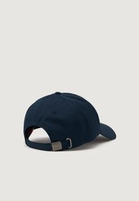 Marineblå baseball cap med buet skjerm, justerbar stropp bak og en metalldetalj. Har stikt detaljer på kronen.