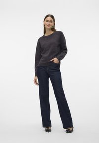Maglione di lana grigio scuro con scollatura rotonda, abbinato a jeans in denim scuro a gamba dritta. Il modello si trova su uno sfondo bianco semplice.
