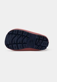 Suola di una scarpa con un modello di battistrada spesso nero e un'intersuola rossa, mostrata su uno sfondo bianco semplice.