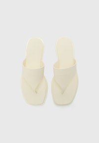 Calvin Klein flip-flops in light cream, featuring a smooth, molded footbed and a V-shaped strap design with embossed logo.