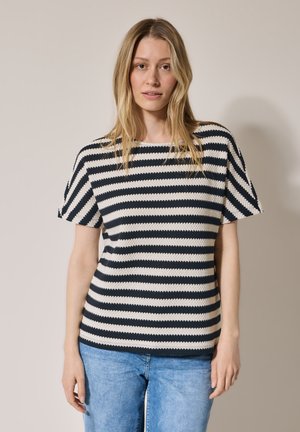 Pull en tricot rayé bleu marine et crème, à manches courtes et col rond. Texture douce et coupe décontractée. Porté avec un jean bleu clair.