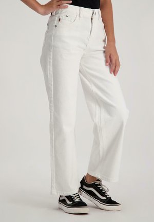 Witte denim wijde broek met hoge taille, voorzien van voorkruisen en een ritssluiting, gedragen met zwart-witte sneakers.
