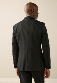 Black tailored suit jacket with a smooth finish, single vent at the back, and buttoned cuffs. Features a classic lapel design.
